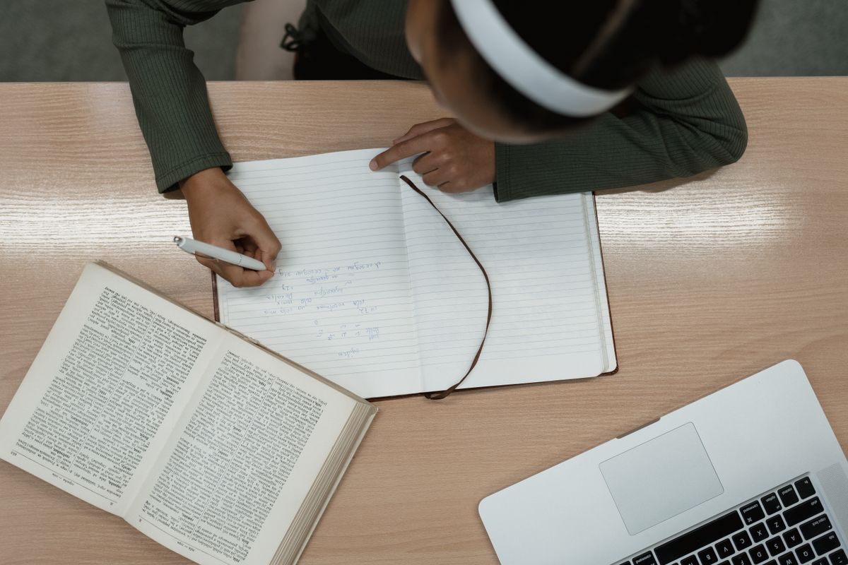 Top-down view of a student writing RBT study notes in a notebook beside a textbook and laptop